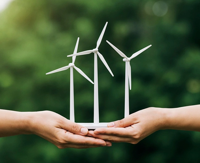 Handen die miniatuur windturbines vasthouden, symbool voor milieuvriendelijke verantwoordelijkheid, adoptie van schone energie en duurzame ontwikkeling.